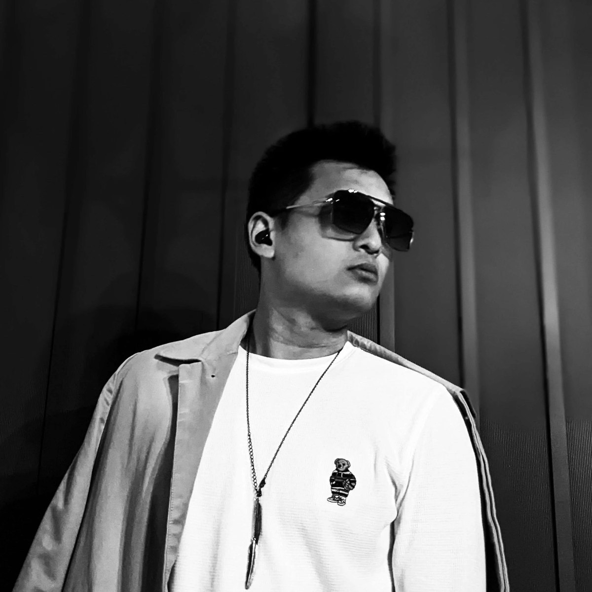 Colin Lin in sunglasses, a white tee and an open jacket, looking off to the side